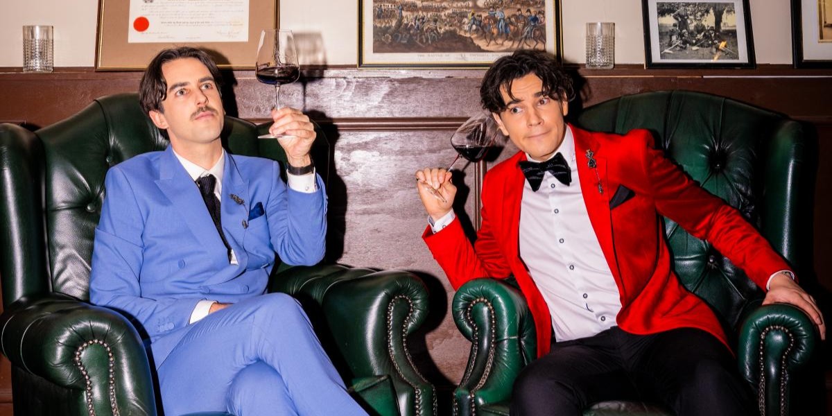 Sweeney Preston and Ethan Cavanagh sit in suits on swanky leather chairs, with wineglasses as props.