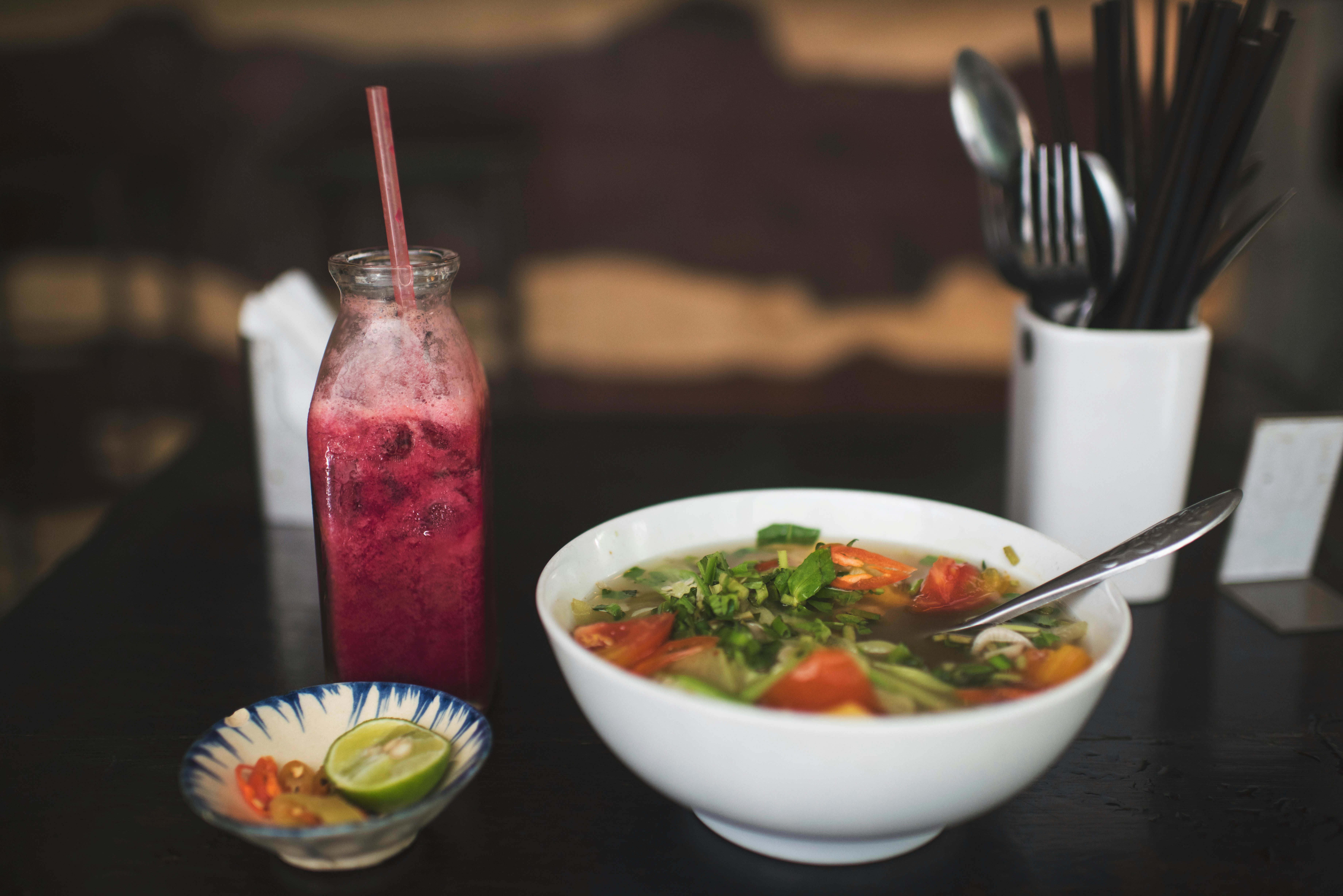 Bowl of noodles with green garnish, spoon and berry smoothie on a wooden table