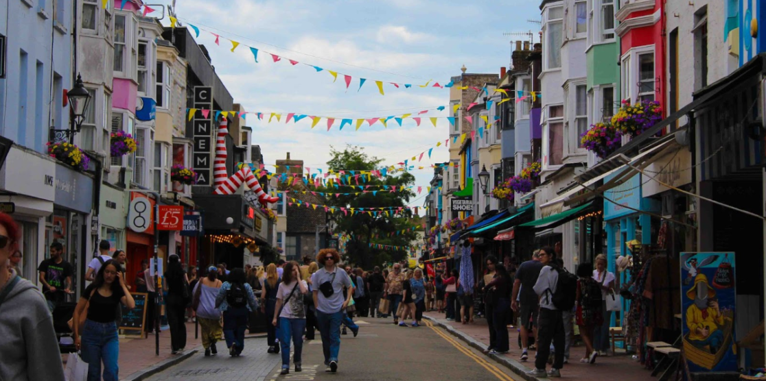 Gardner Street in the North Laine, Brighton - people can be seen walking in the street between two rows of shops with colourful bunting ties between the shops.